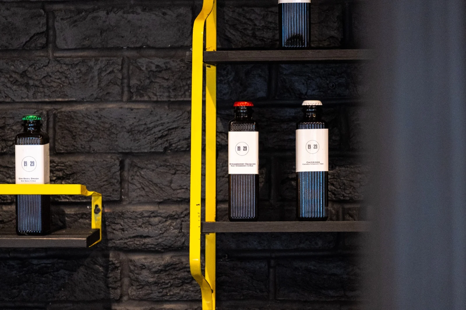 19/29 bottles on yellow shelves against a black brick wall