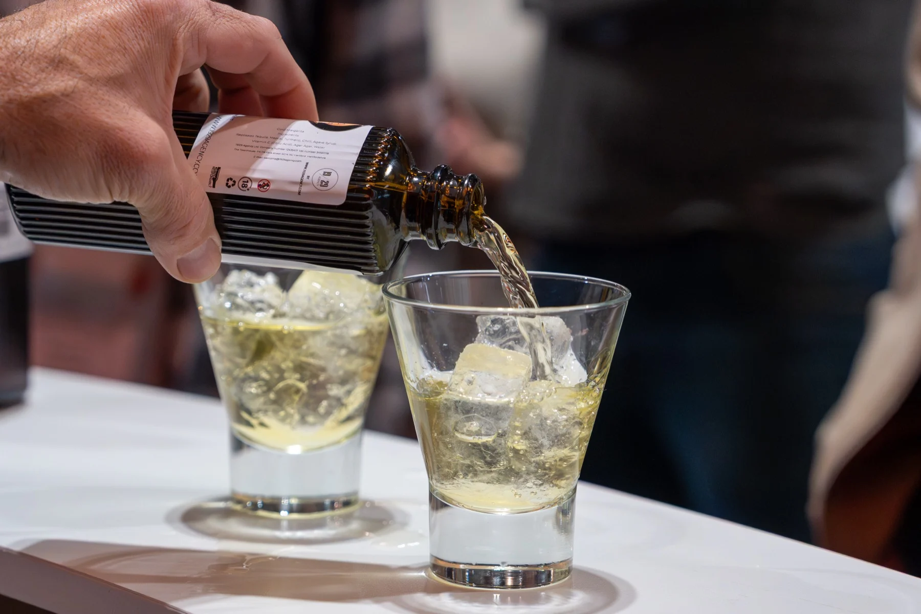 A 19/29 cocktail being poured over ice into two tumblers on the bar