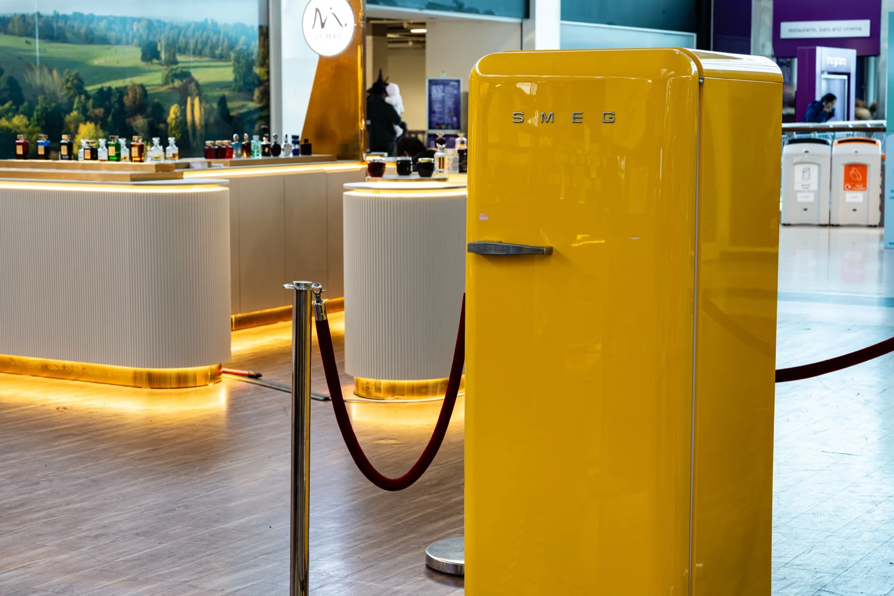 A yellow fridge beside velvet rope barriers at the pop-up
