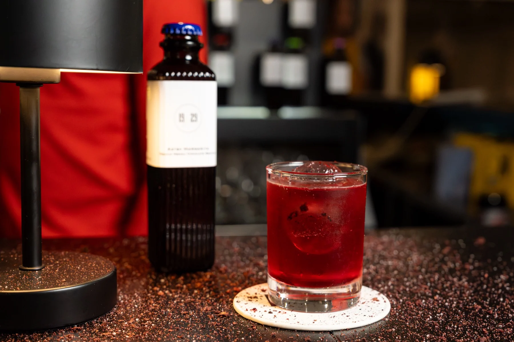A red cocktail beside a 19/29 bottle on the bar